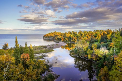 A serene landscape featuring a river winding through vibrant autumn trees, reflecting clouds and colors in the water.