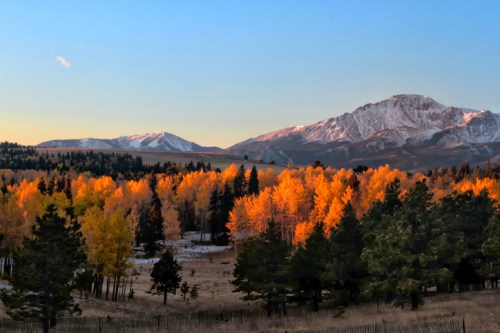 A scenic view of mountains with snow, surrounded by vibrant autumn trees in shades of orange and yellow.