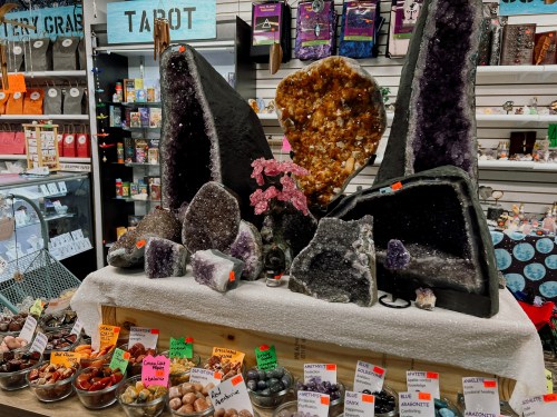 A display of various crystals and geodes in a shop, with colorful labels and a variety of stones on a table.
