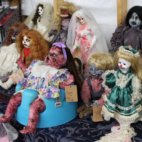 A collection of creepy dolls displayed on a table, featuring various styles and eerie facial expressions.