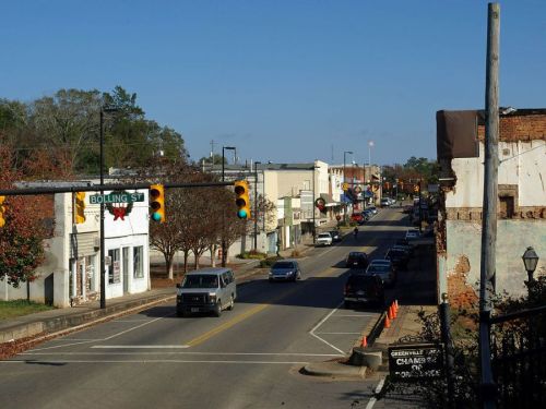 A view of a small town street with shops, traffic lights, and parked cars under a clear blue sky.