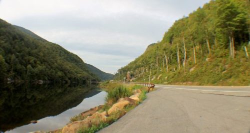 A serene landscape featuring a calm lake surrounded by lush green hills and a winding road.