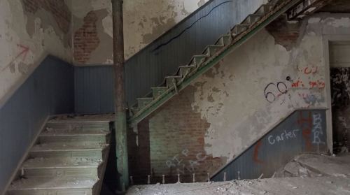 An abandoned staircase with peeling paint and graffiti on the walls, showcasing a worn, neglected interior.