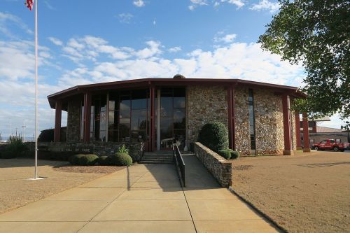 Exterior view of a stone building with large windows, featuring a flagpole and landscaped entrance.