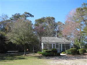 A small house surrounded by trees and shrubs, with a clear blue sky above and picnic tables nearby.