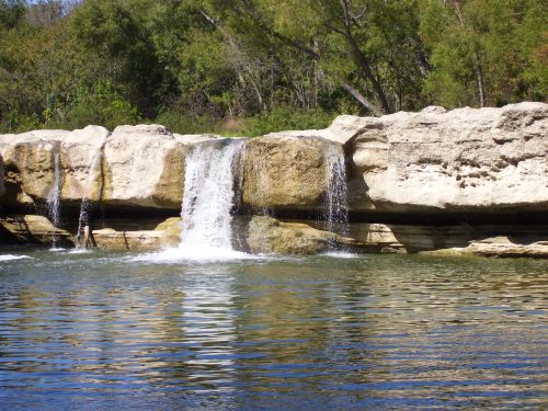 A serene waterfall cascading over rocky cliffs into a calm, reflective pool surrounded by lush greenery.