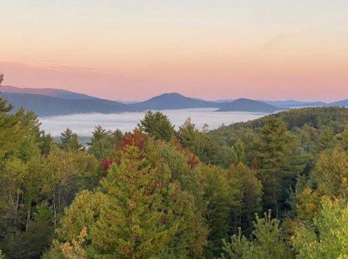 A serene landscape of mountains and trees at sunrise, with mist hovering over the valleys below.