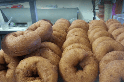 A close-up of a stack of golden-brown, freshly made donuts arranged on a tray.