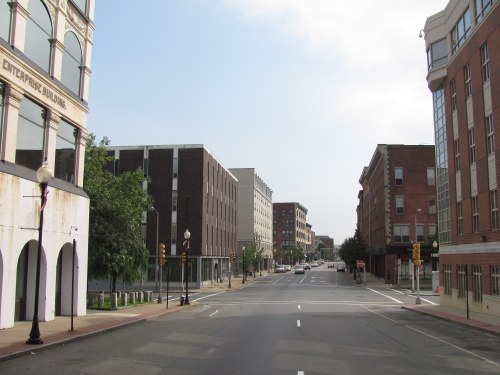 A quiet city street lined with buildings, featuring a mix of architectural styles and clear blue skies.