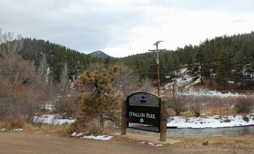 Sign for O'Fallon Park near a snowy landscape with trees and mountains in the background.