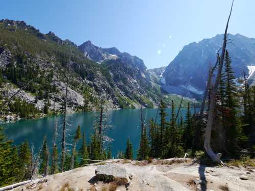 A serene mountain lake surrounded by lush greenery and towering peaks under a clear blue sky.