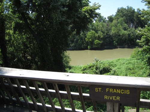 View of the St. Francis River from a wooden deck, surrounded by lush greenery and trees.