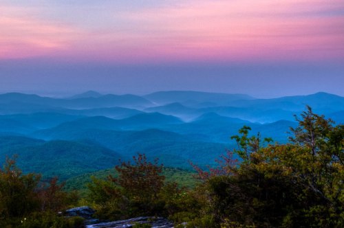 A serene mountain landscape at dusk, featuring rolling hills and a colorful sky with soft pink and blue hues.