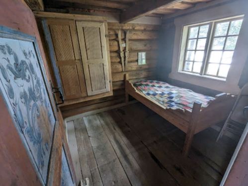 Cozy wooden interior of a rustic room featuring a bed with a patchwork quilt and a window letting in natural light.