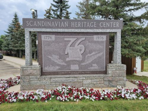 Sign for the Scandinavian Heritage Center, featuring dates 1776 and 1976, surrounded by flowers and trees.