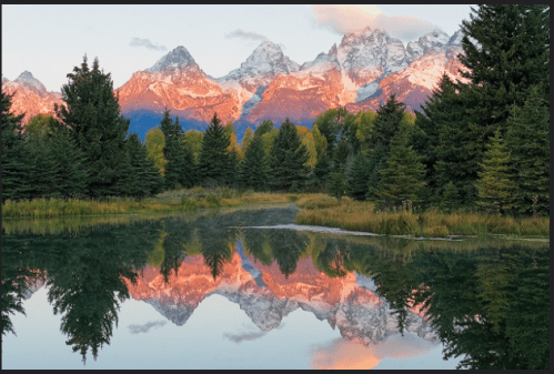 A serene landscape featuring mountains reflecting in a calm lake, surrounded by lush trees and a colorful sunset sky.