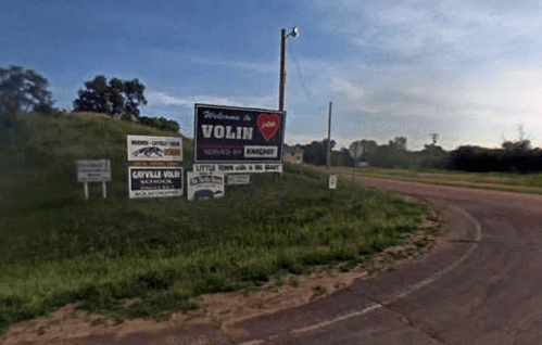 Welcome sign for Volin, South Dakota, with various local business advertisements along a winding road.