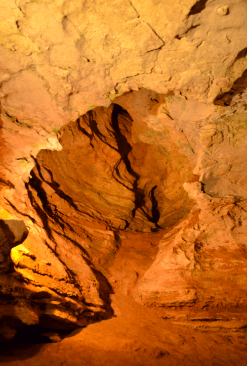 A dimly lit cave interior with textured rock formations and earthy tones, showcasing natural erosion patterns.