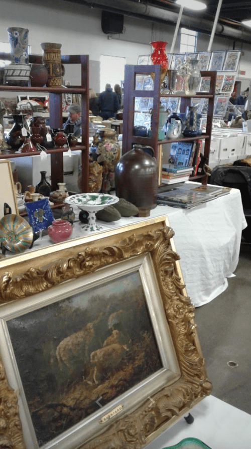 A bustling antique market with various items for sale, including paintings, pottery, and decorative glassware.