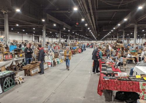 A bustling indoor market with vendors and shoppers browsing various handmade goods and crafts.