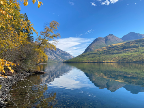 A serene lake surrounded by mountains, with autumn foliage and clear blue skies reflecting on the water's surface.