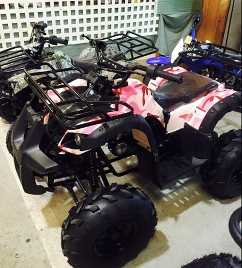 A pink and black ATV parked in a garage, surrounded by other vehicles and equipment.