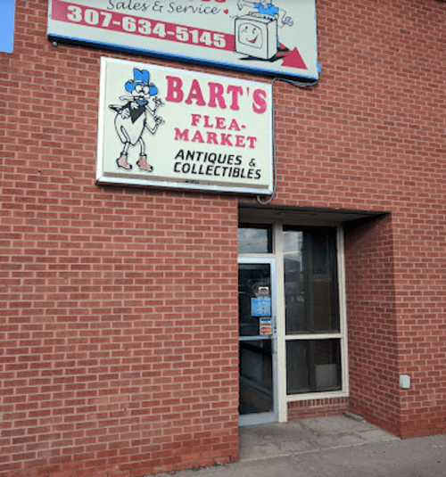 Sign for Bart's Flea Market, featuring antiques and collectibles, on a brick building with a glass door.