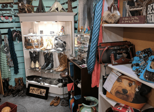 A cozy boutique display featuring boots, handbags, and various accessories on shelves and in glass cases.