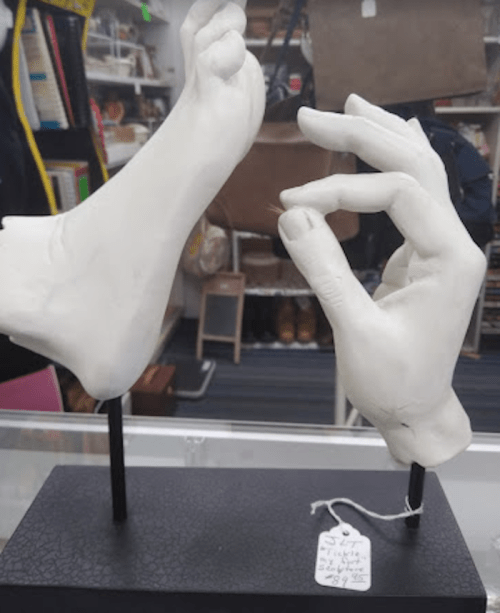 A sculptural display featuring a foot and a hand, both in white, mounted on a black base.