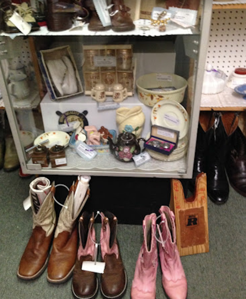 A display case filled with vintage items, featuring various dishes, a teapot, and two pairs of boots in the foreground.