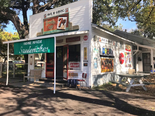 A small, charming grocery store with a sign for homemade sandwiches and a vintage soda advertisement outside.