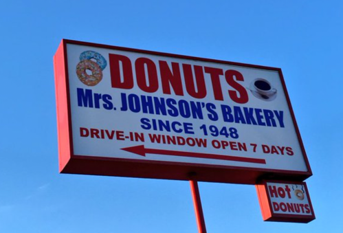 Sign for Mrs. Johnson's Bakery featuring "Donuts" and "Drive-In Window Open 7 Days," established in 1948.