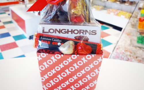 A gift basket with chocolates and candies, featuring a "Longhorns" card, set against a colorful candy store background.