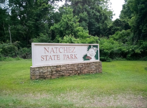 Sign for Natchez State Park, featuring greenery and trees in the background.