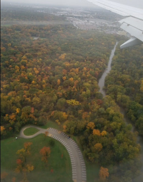 Aerial view of colorful autumn trees, a winding river, and a parking lot below, with a plane wing in the corner.