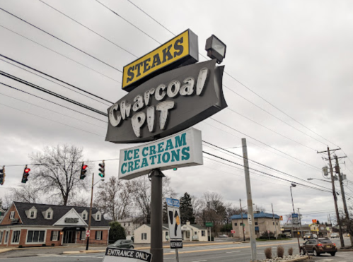Sign for Charcoal Pit featuring "Steaks" and "Ice Cream Creations," with a cloudy sky in the background.