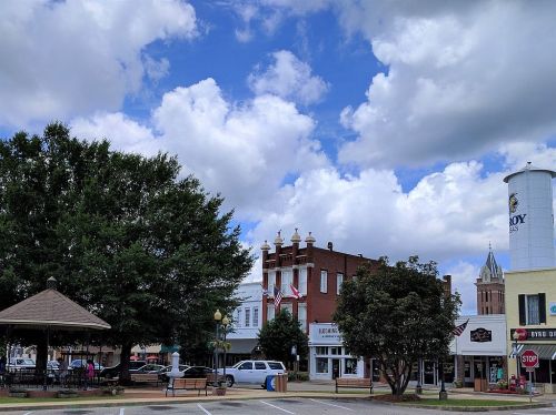 A small town square with a gazebo, trees, and buildings under a partly cloudy sky.