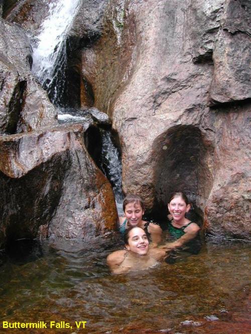 Three people enjoy a swim in a natural pool at Buttermilk Falls, surrounded by rocky cliffs and a waterfall.