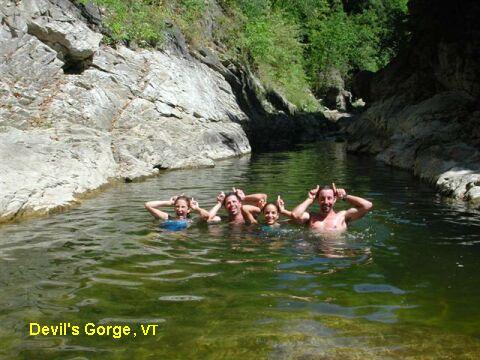 Four people playfully pose in a natural pool at Devil's Gorge, VT, surrounded by rocky cliffs and greenery.