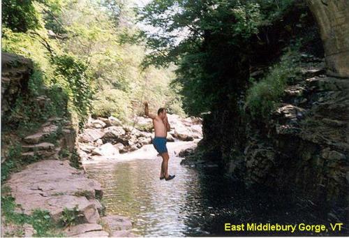 A person jumps into a river surrounded by rocky cliffs and lush greenery in East Middlebury Gorge, VT.