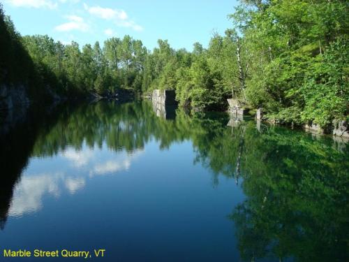 A serene quarry lake surrounded by lush greenery, reflecting trees and cliffs in calm water. Marble Street Quarry, VT.