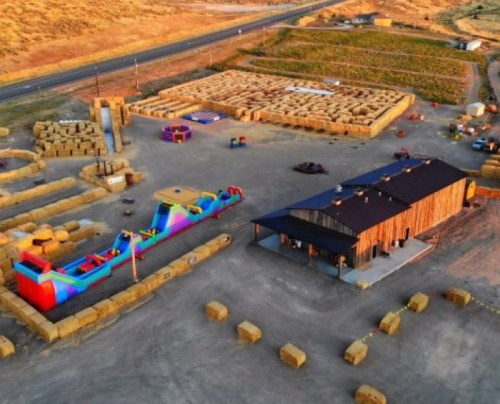 Aerial view of a colorful inflatable slide and a rustic building surrounded by hay bales and open land.