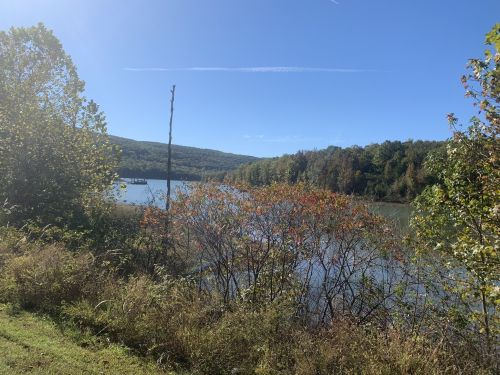A serene landscape featuring a calm lake surrounded by trees and hills under a clear blue sky.