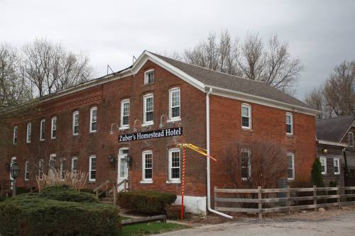 A brick building with a sign reading "Zuber's Homestead Hotel," surrounded by trees and a wooden fence.