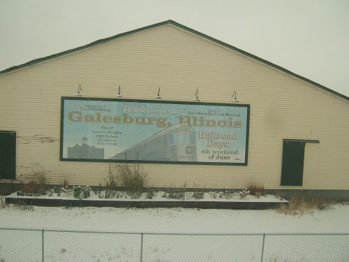 Sign welcoming visitors to Galesburg, Illinois, featuring a train and promoting Railroad Days in June. Snowy setting.