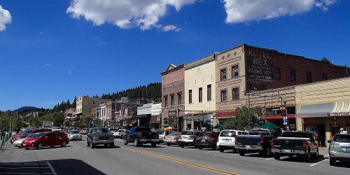 A charming small-town street lined with historic buildings, shops, and parked cars under a blue sky with fluffy clouds.