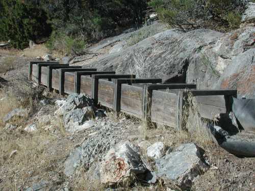 A series of wooden boxes lined along a rocky terrain, surrounded by dry grass and shrubs.