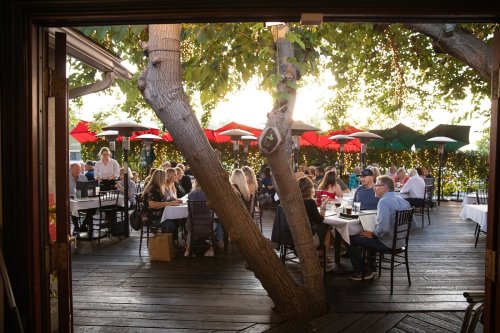 A lively outdoor restaurant scene with diners at tables under colorful umbrellas, surrounded by greenery and warm lighting.