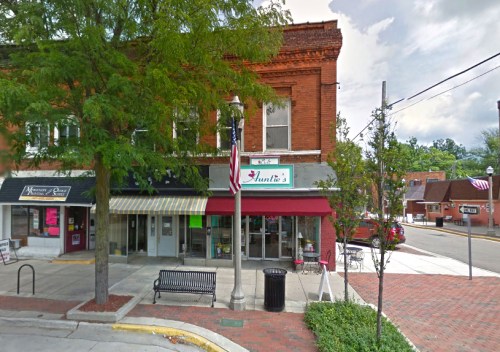 A street view of a small town with shops, including "Hunter's," and trees lining the sidewalk.
