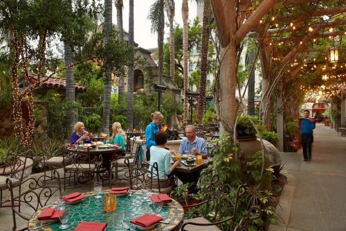 Outdoor dining area with tables, surrounded by greenery and string lights, as guests enjoy their meals.